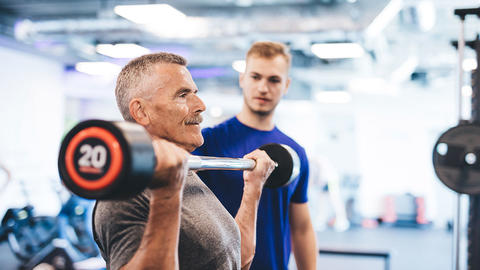 Mann macht unter Anleitung des Trainers Kraftübungen