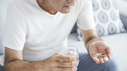 Mann nimmt auf dem Sofa Medikamente ein