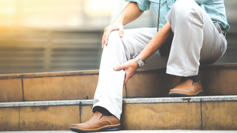 Mann fasst sich mit der Hand ans Bein