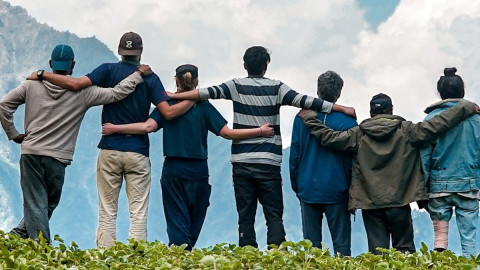 Junge Menschen stehen Arm in Arm auf einem Berggipfel und genießen die Aussicht.